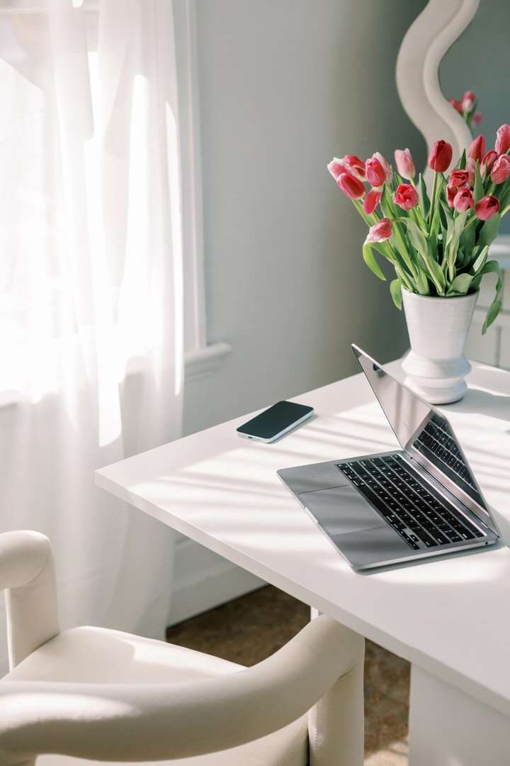 A stylish laptop alongside a lovely flower vase on a pristine white desk, blending technology with a hint of nature.