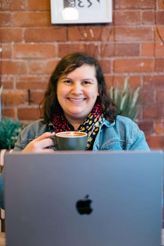 Lyndsey smiling with hot chocolate and laptop in Hereford cafe